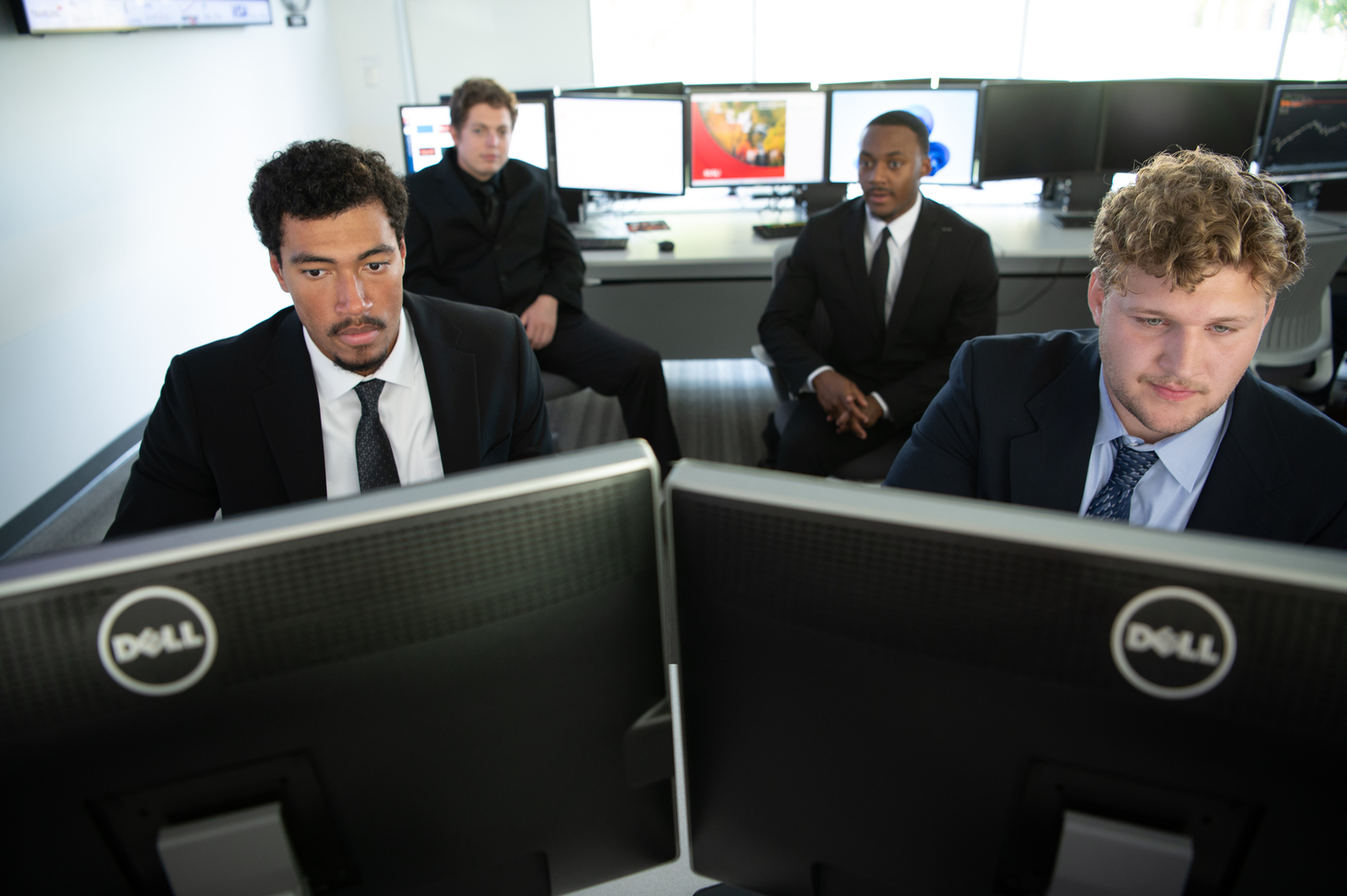 four students in suits looking at computer screen